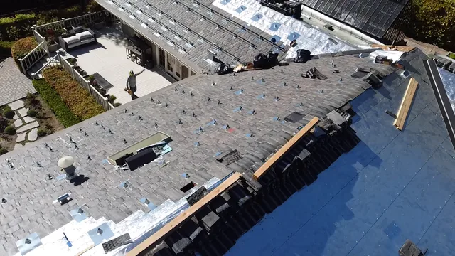 Tile roof underlayment being installed beneath lifted tiles