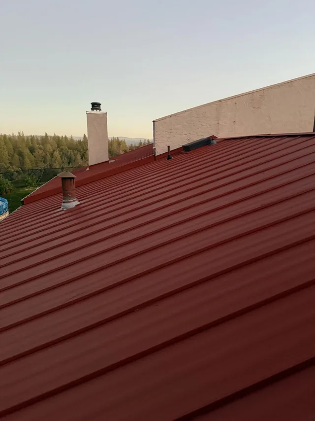 Red standing seam roof panels around a chimney